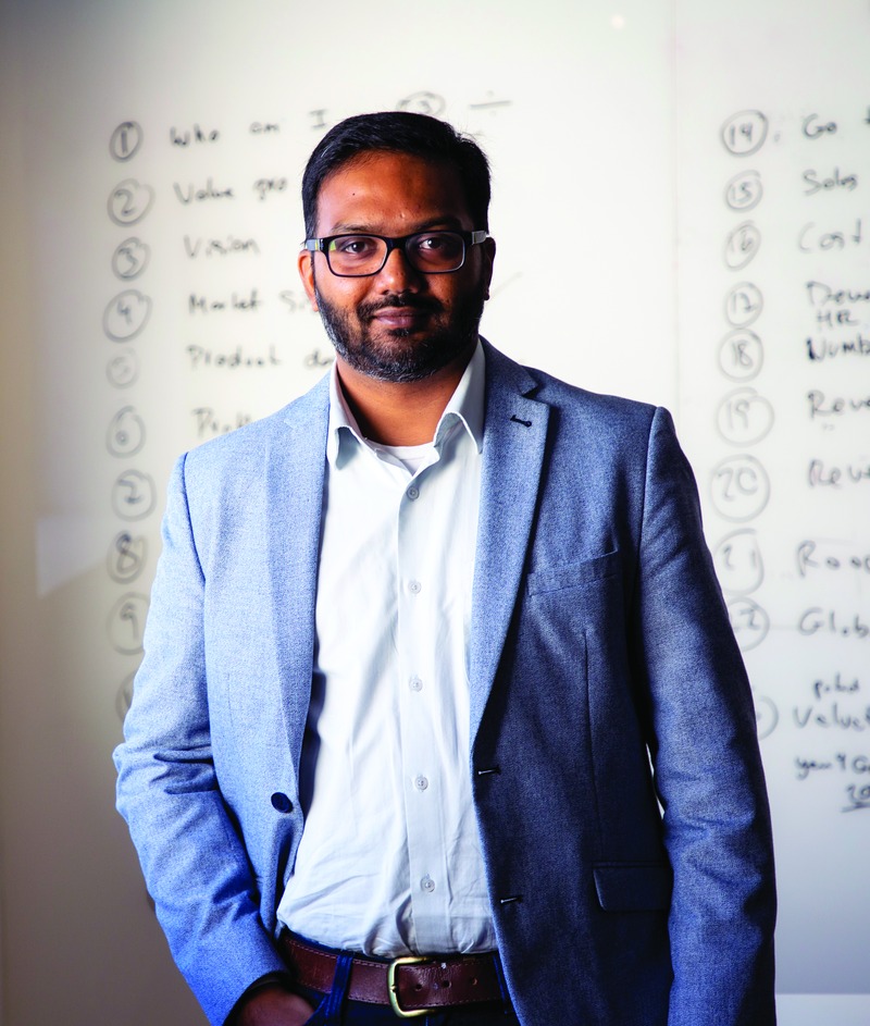 Suhit Anantula in a blue blazer, standing in front of a whiteboard